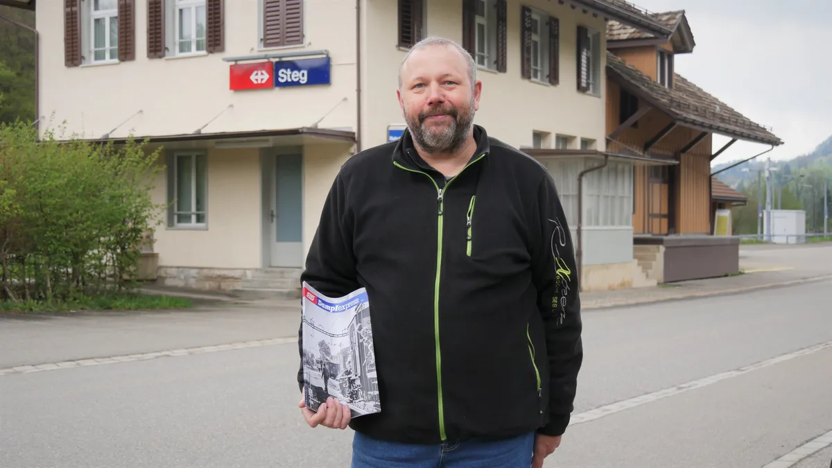 Man sieht einen Herrn mittleren Alters, der vor einem Bahnhofgebäude steht und ein Magazin in den Händen hält.